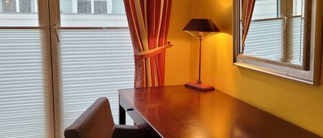 Une chambre d’hôtel avec un bureau en bois, une chaise, une lampe et un grand miroir.