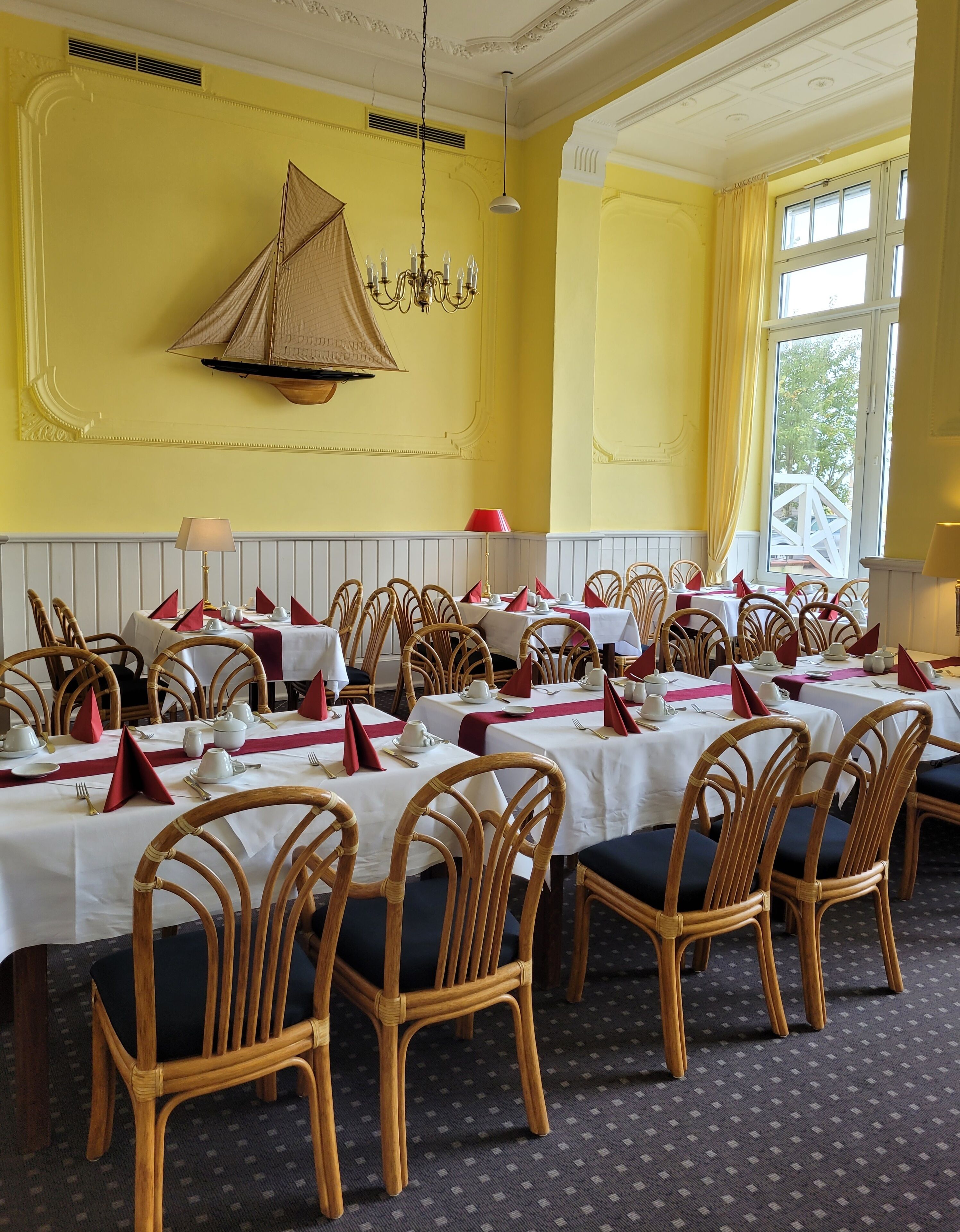 A dining area with multiple tables set for service, wicker chairs, and a yellow wall with a decorative element.