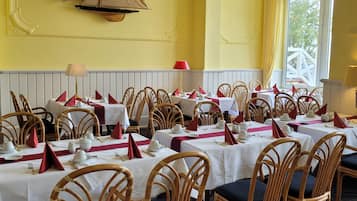 A dining area with multiple tables set for service, wicker chairs, and a yellow wall with a decorative element.