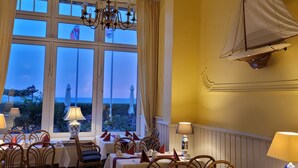 Un espace repas avec des tables dressées, de grandes fenêtres offrant une vue agréable et un lustre.