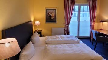 Habitación de hotel con una cama grande, dos mesitas de noche, un escritorio y una ventana con cortinas.