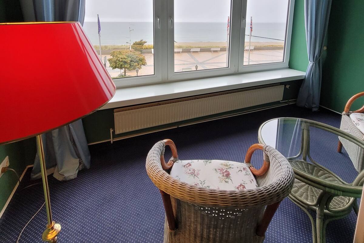 A room with a large window, wicker chairs, a red lamp, and a radiator.
