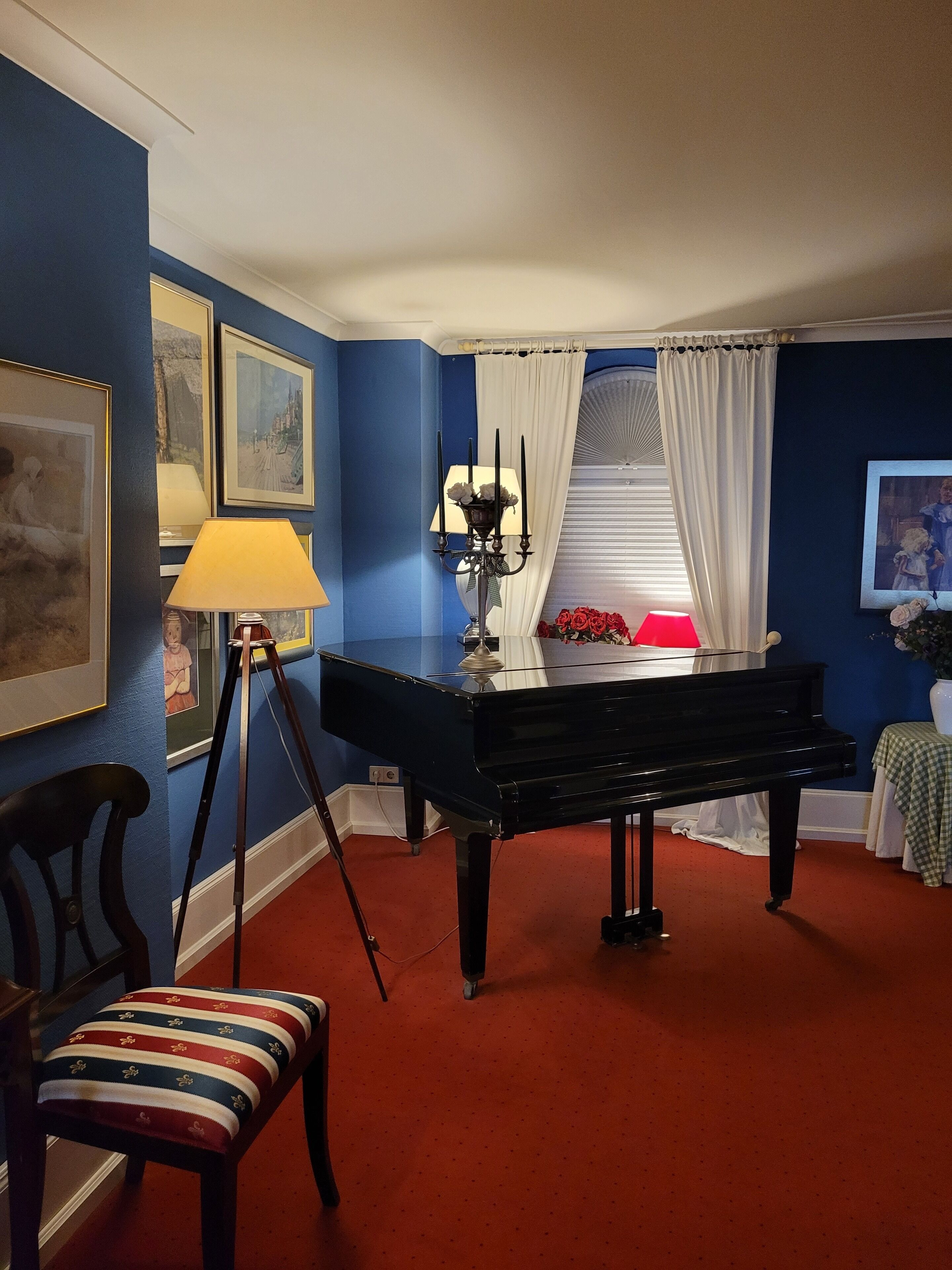 Une pièce avec un grand piano, un lampadaire sur trépied et une chaise dotée d’un coussin à rayures.