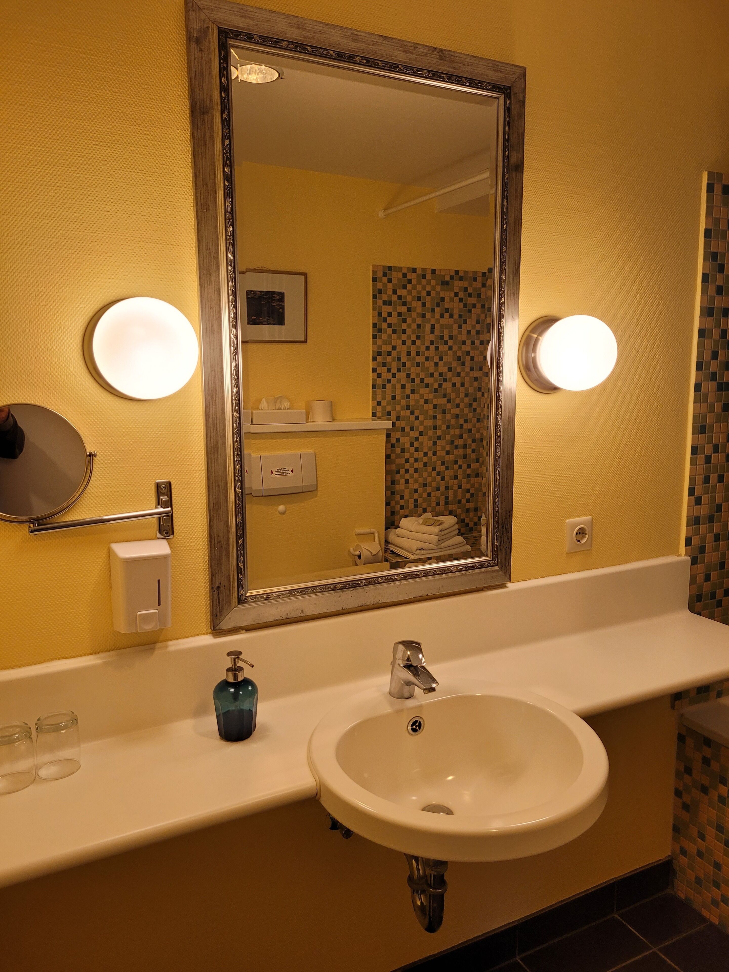 Une salle de bain avec un grand miroir, un lavabo et deux appliques murales.