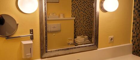 Une salle de bain avec un grand miroir, un lavabo et deux appliques murales.
