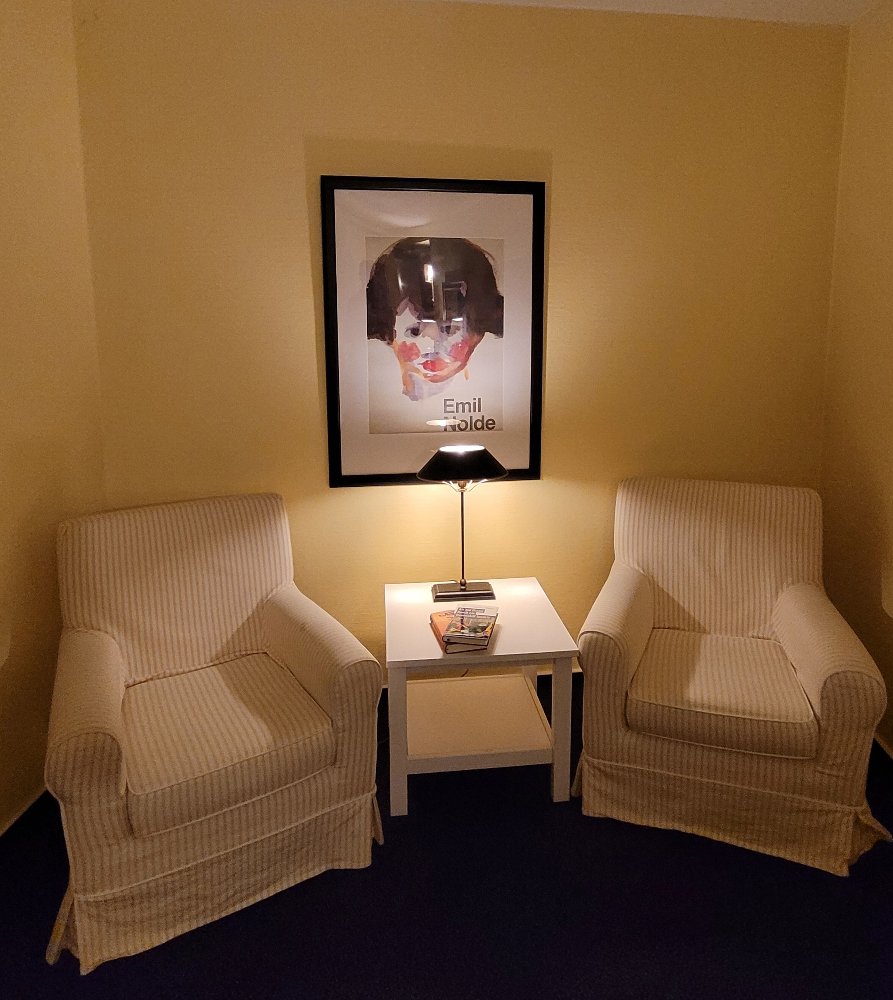 A room with two striped armchairs, a small table with a lamp, and a framed picture on the wall.
