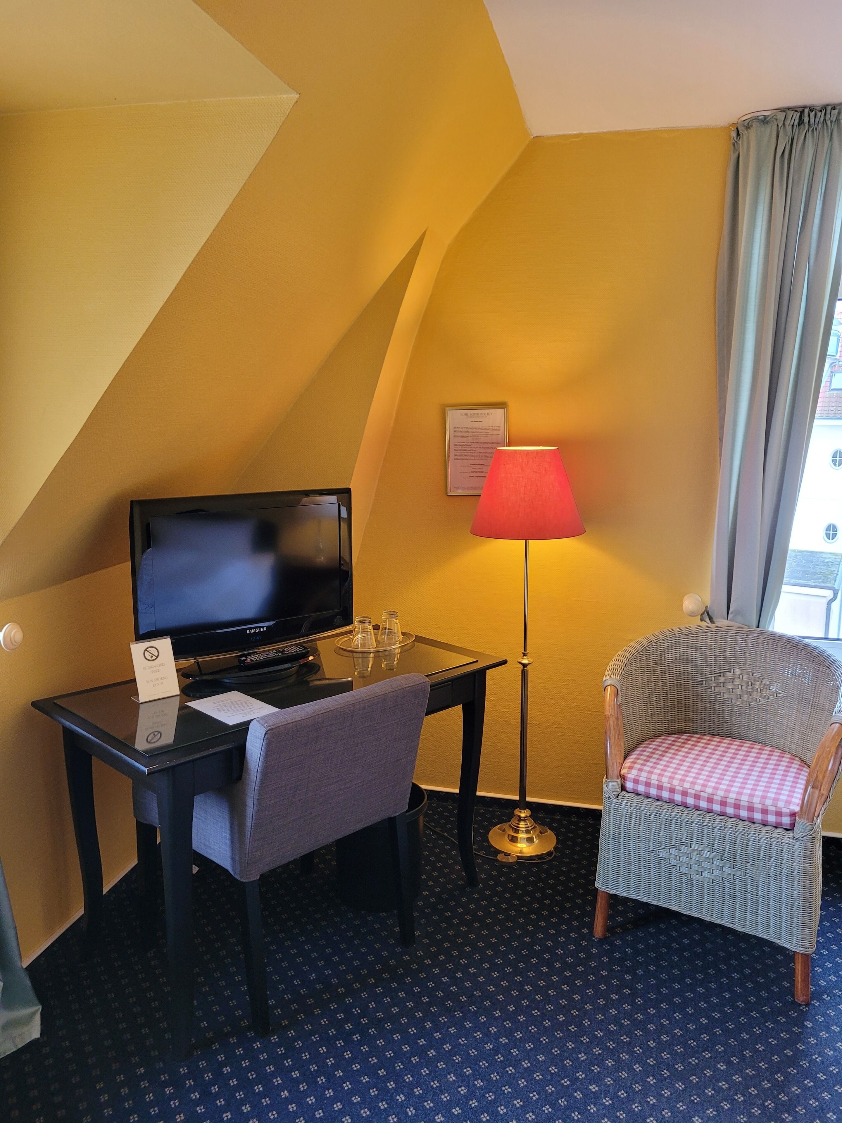 Une chambre d’hôtel équipée d’un bureau, d’une télévision, d’une lampe, d’une chaise et d’un tapis à motifs.