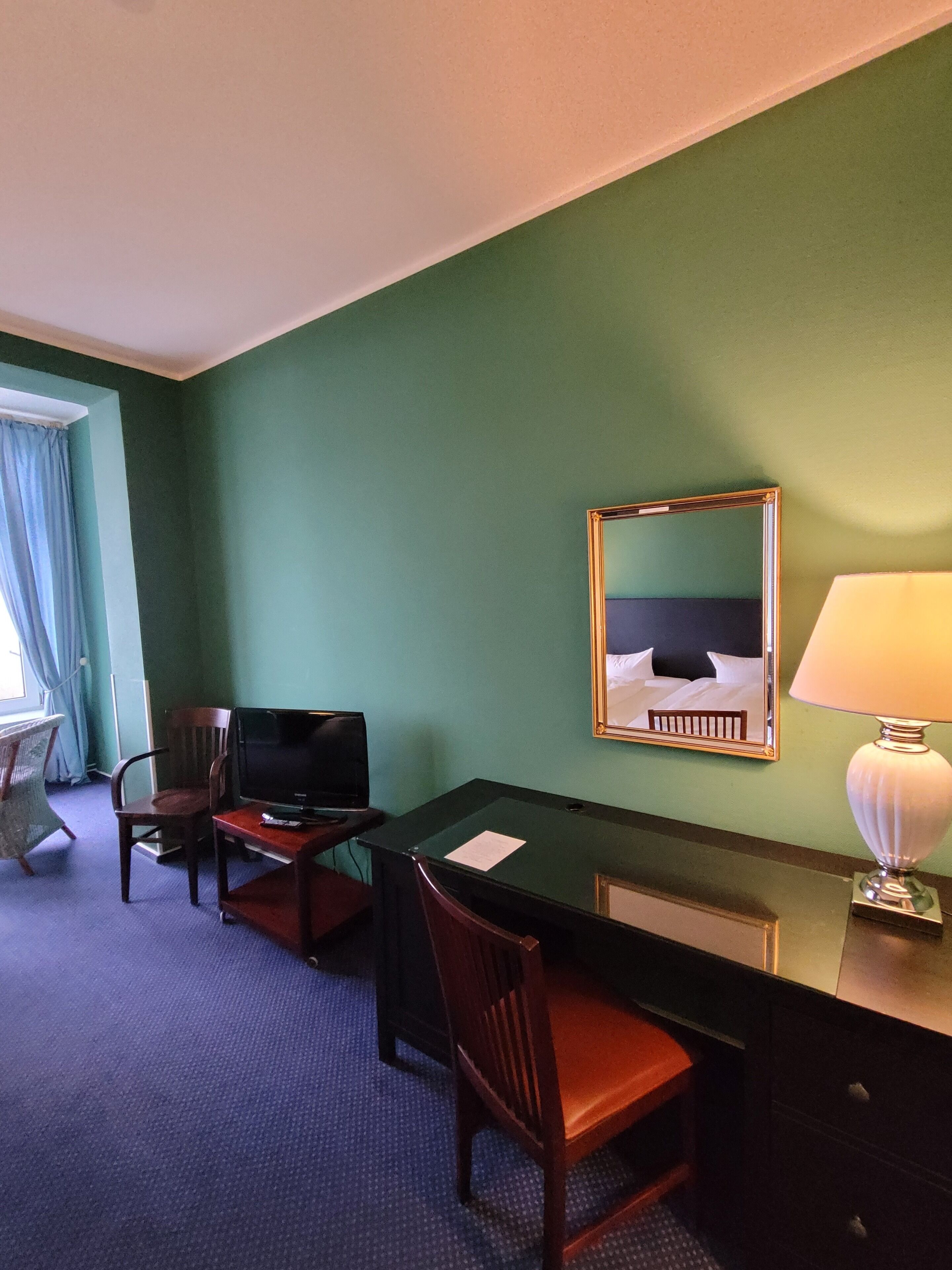 Ein Hotelzimmer mit Schreibtisch, zwei Stühlen, Fernseher, Bett und Lampe.