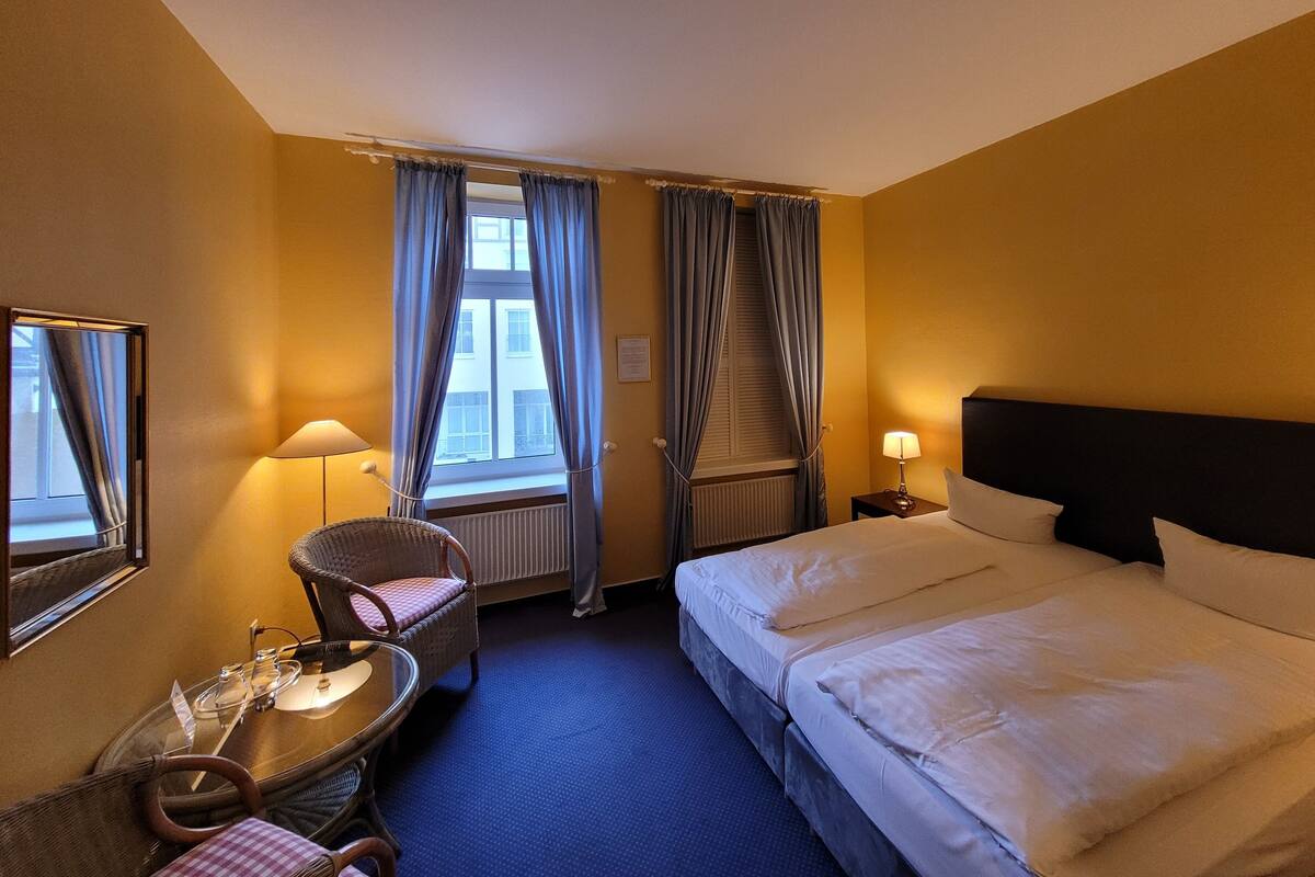 A hotel room with a bed, a chair, a table, and a window with curtains.