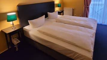 Ett hotellrum med en stor säng, två sängbord, en grön lampa, en telefon och ett fönster med gardiner.