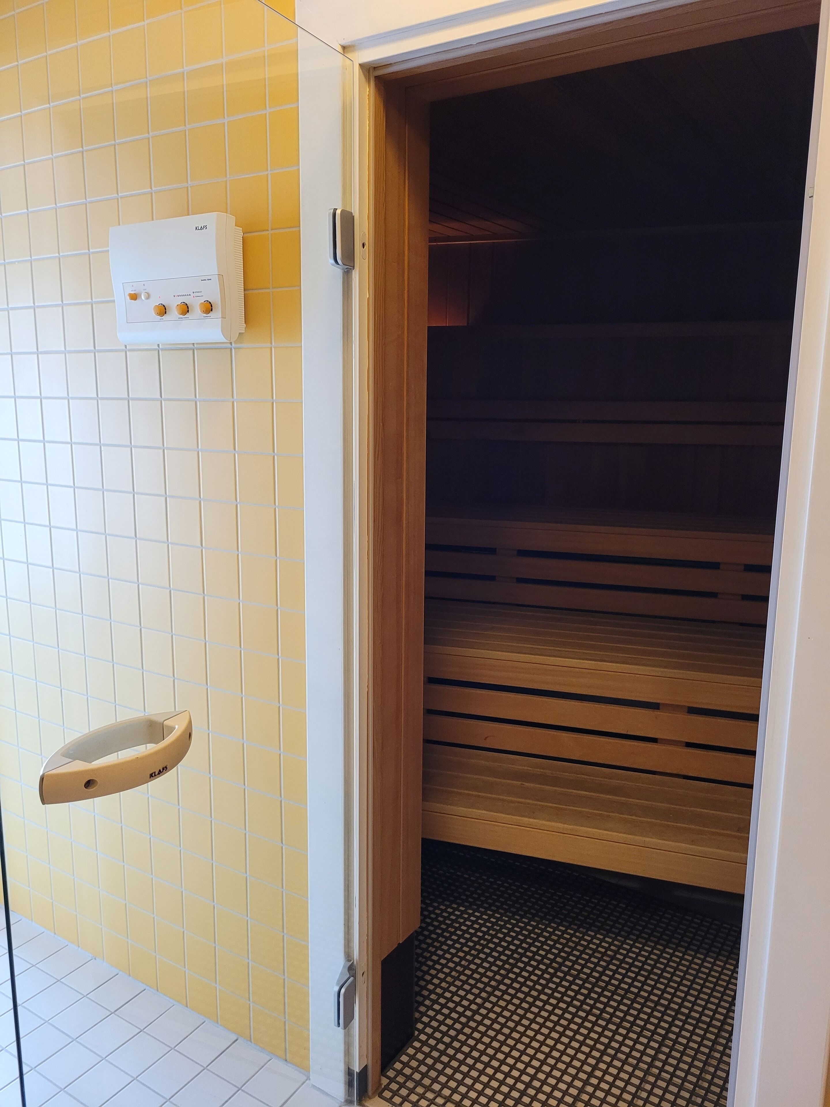 A bathroom with a tiled wall, a white towel rack, and a wooden door leading to a shower area.