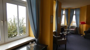 Une chambre d’hôtel avec une grande fenêtre, un bureau avec un ordinateur, une chaise et une petite table avec un verre.