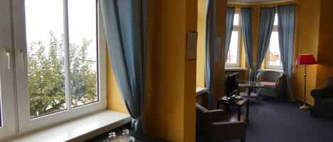 A hotel room with a large window, a desk with a computer, a chair, and a small table with a glass.