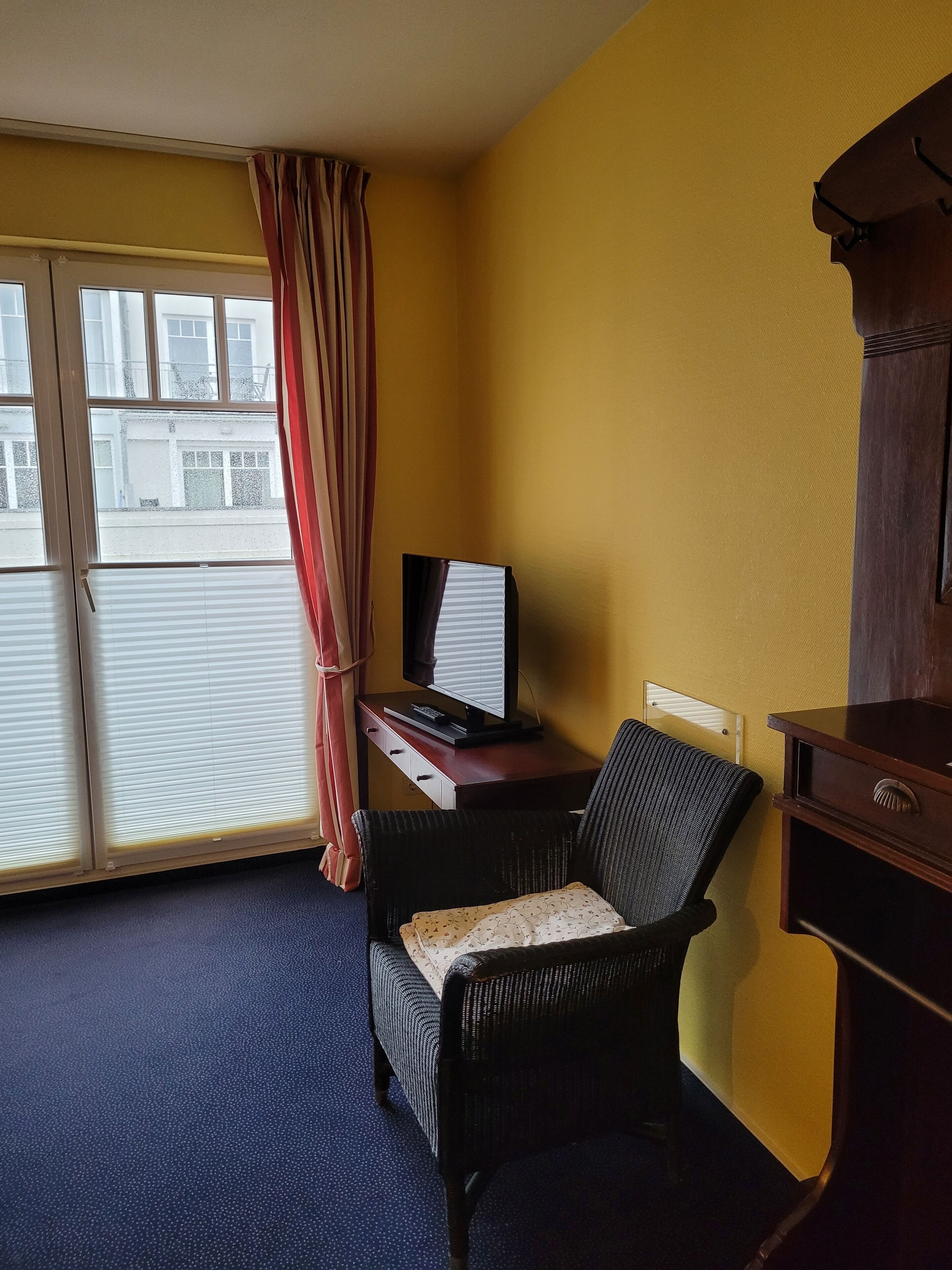 Une chambre d’hôtel avec une grande fenêtre, un bureau équipé d’un ordinateur, une chaise et un petit meuble de rangement.