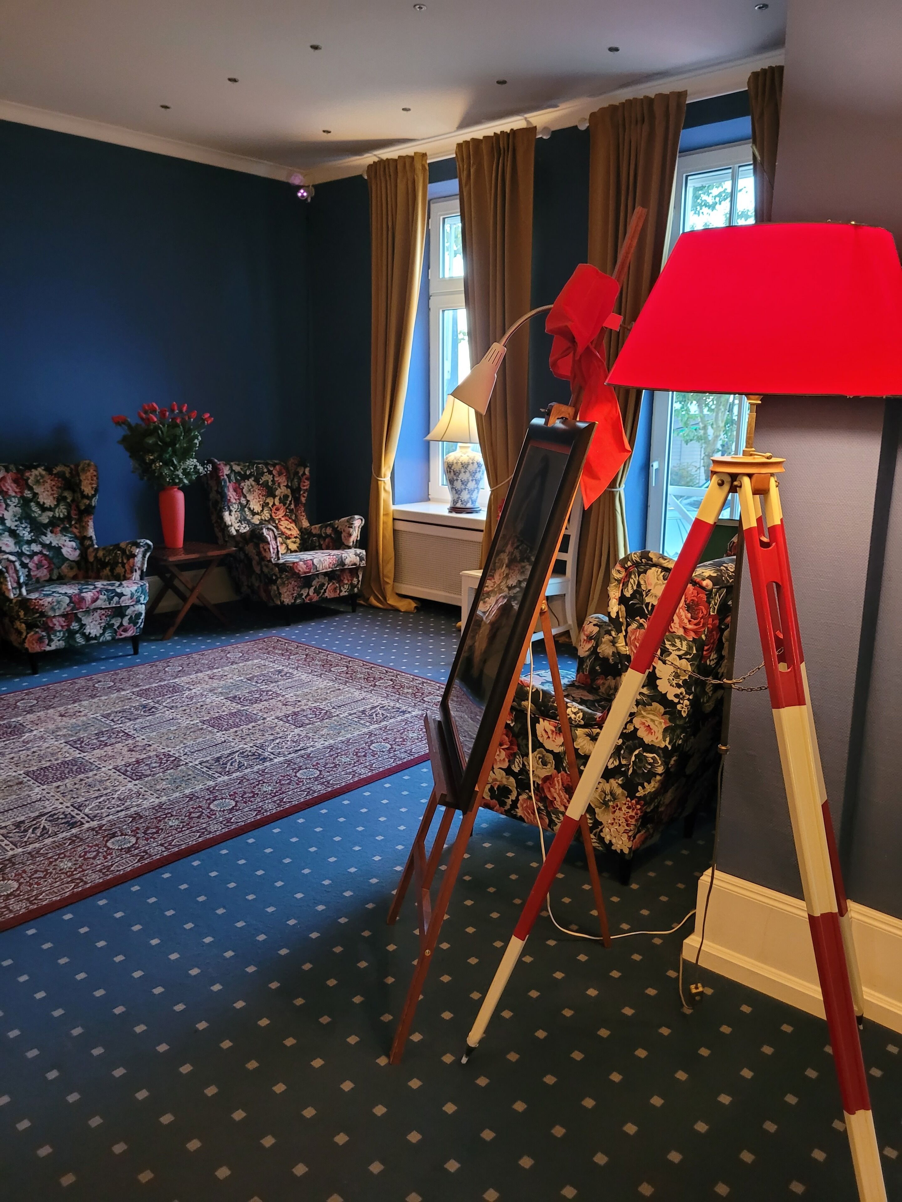 A living room with floral-patterned furniture, a red lamp, and a tripod stand.