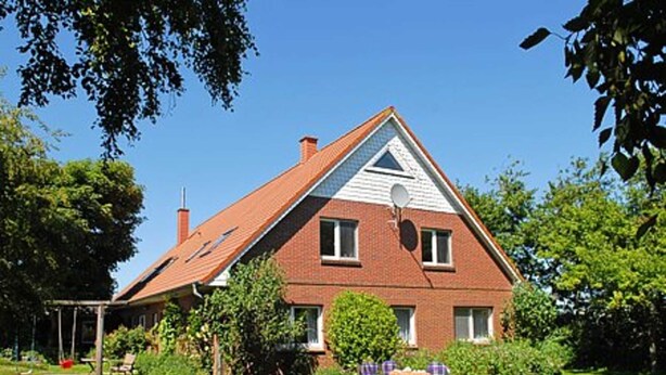 A two-story house with a sloped roof, a chimney, and a small porch with a table and chairs.