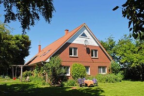 A two-story house with a sloped roof, a chimney, and a small porch with a table and chairs.