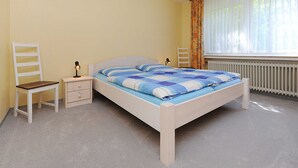 A bedroom with a bed, a nightstand, a chair, and a window with curtains.