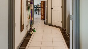 Um corredor com piso de azulejos, uma porta à direita e um espelho à esquerda.