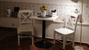 A small dining area with a white table, two white chairs, a floor lamp, and a window with patterned wallpaper.