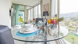 Un coin repas avec une table en verre, de l’assiette blanche et une vue sur la ville et les montagnes.