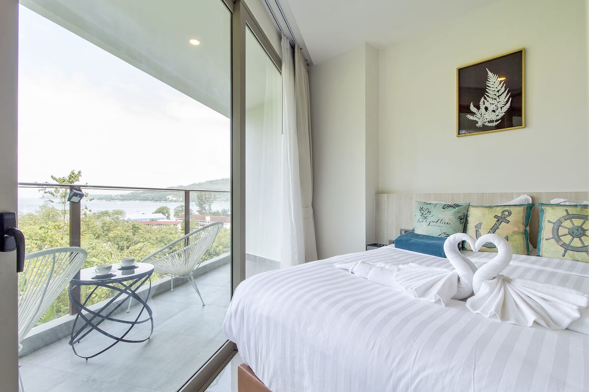 A hotel room with a balcony, a bed with white bedding, and nautical-themed pillows.