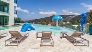 Un espace piscine équipé de chaises longues, d’un toboggan et d’une sculpture représentant un hippocampe.