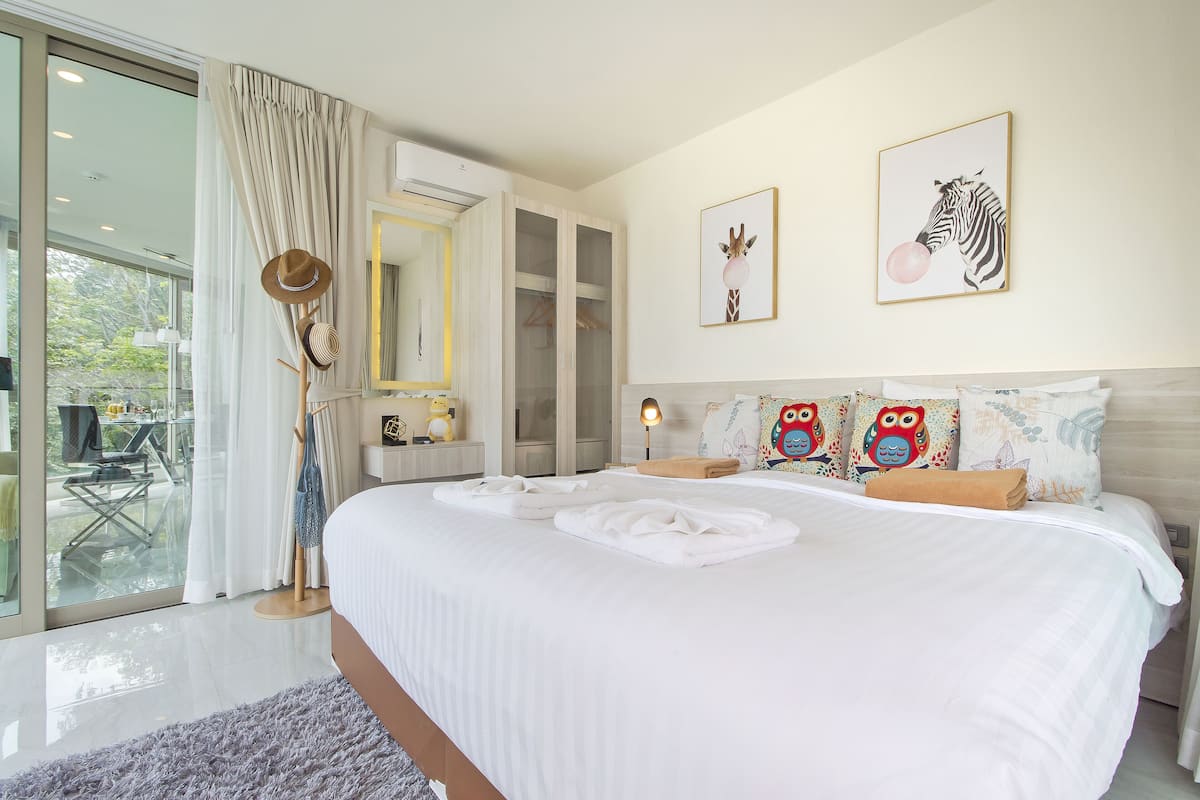 A bedroom with a large bed, a wardrobe, a mirror, and a window with curtains.