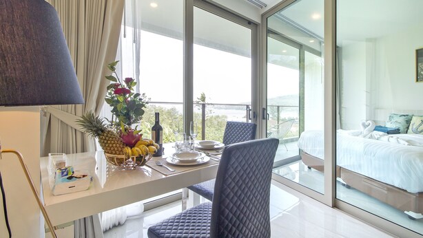 Une chambre d’hôtel moderne avec balcon, un coin repas avec une table dressée pour deux personnes, et un lit offrant une vue agréable.