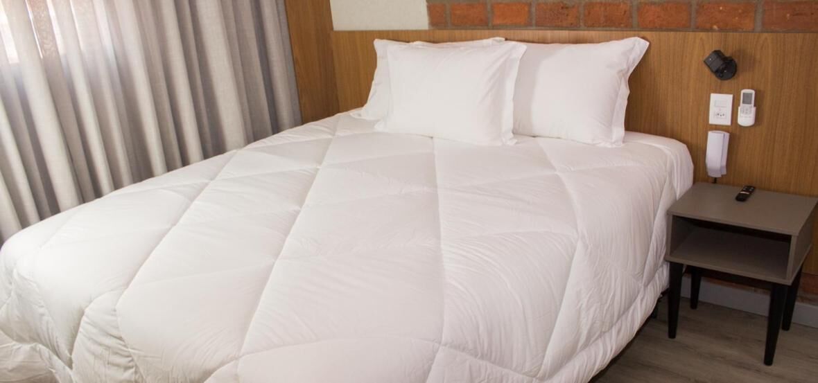A hotel room with a large bed, a wooden headboard, a nightstand with a phone, and a brick wall.