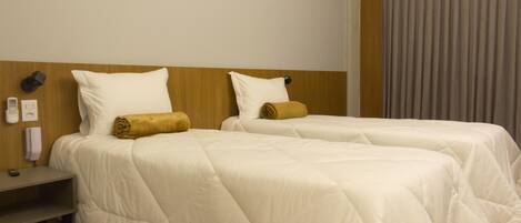 A hotel room with two single beds, a wooden headboard, a desk, and a telephone.