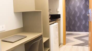 A compact room with a desk, a laptop, a refrigerator, and a patterned wall.