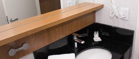 A bathroom with a wooden vanity, a black sink, and two white hair dryers mounted on the wall.
