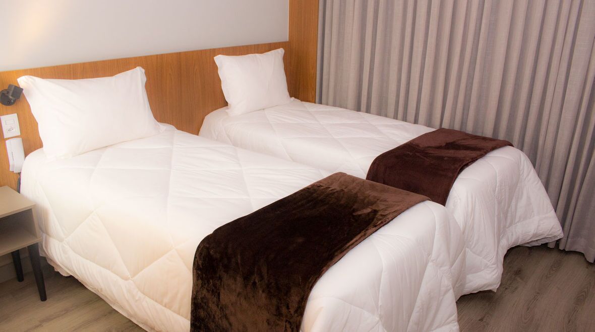 Une chambre d’hôtel avec deux lits, une tête de lit en bois, une table de chevet et un rideau.