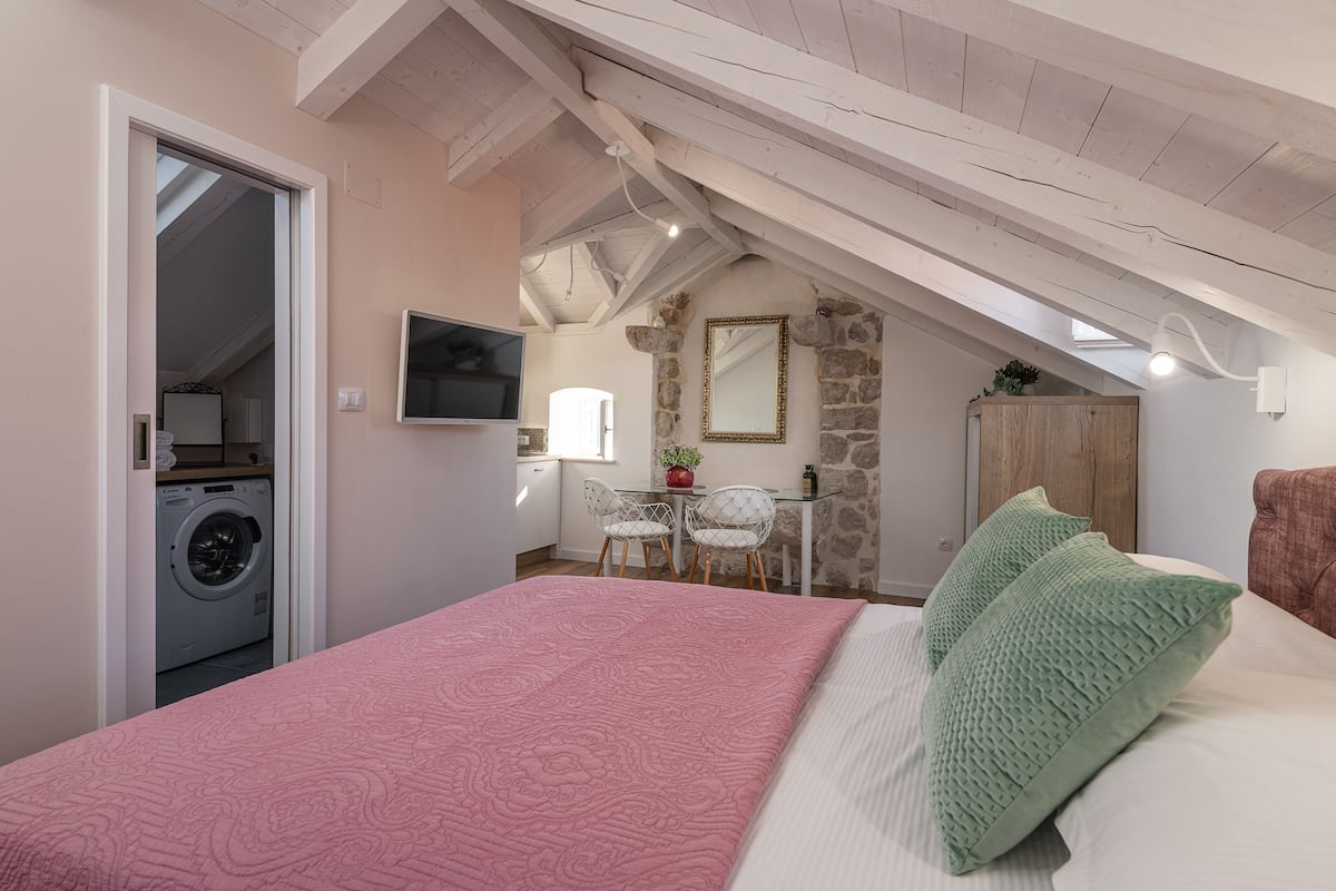 Ein Schlafzimmer mit Bett, Waschmaschine, Schreibtisch und einer Steinwand.