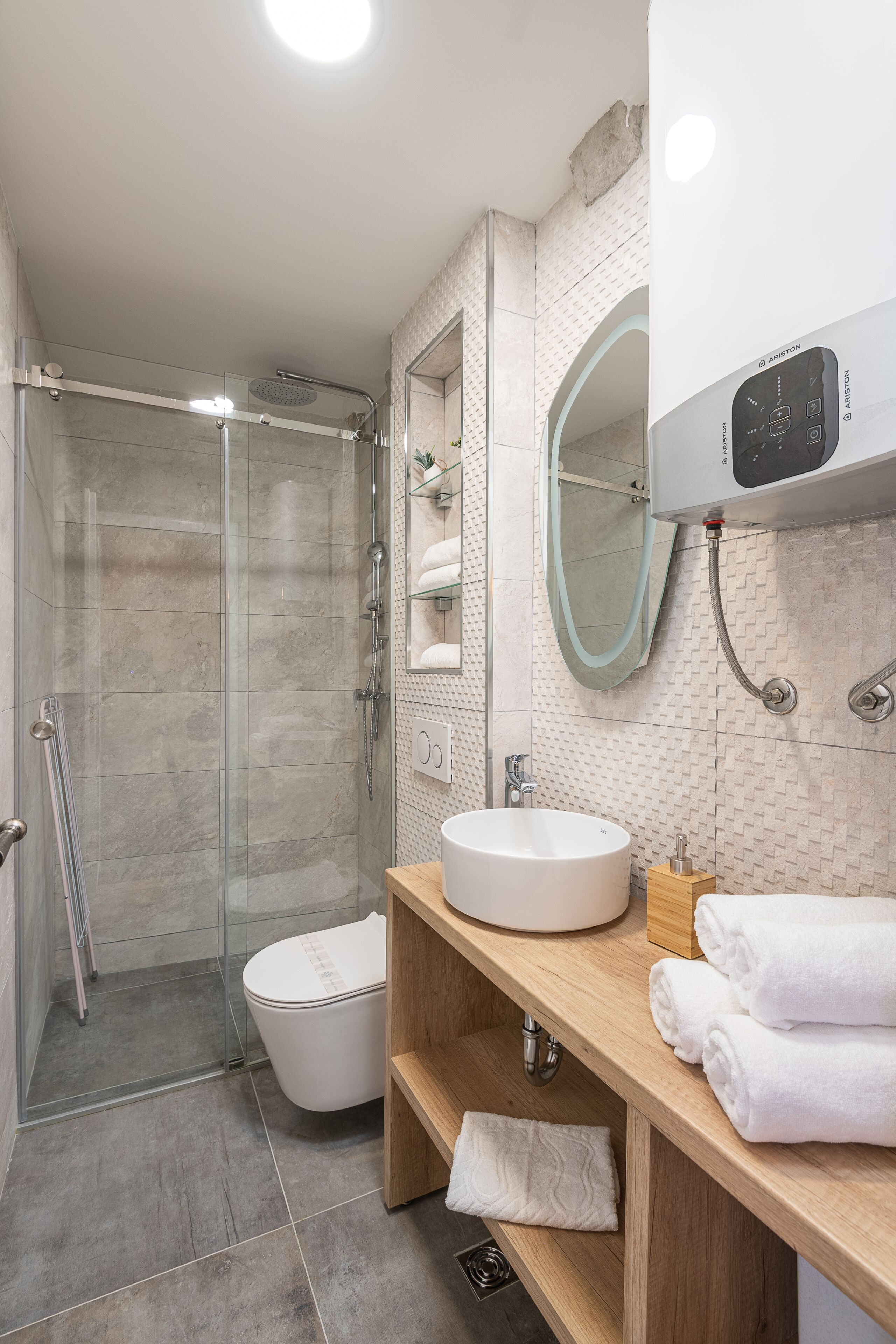 A modern bathroom with a glass-enclosed shower, a white sink, and a wooden vanity with towels.