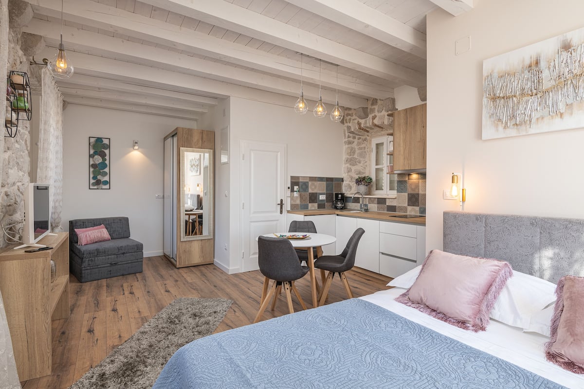 Ein moderner, gut beleuchteter Raum mit einem Bett, einem Esstisch mit Stühlen, einer Couch und einer Küchenzeile.