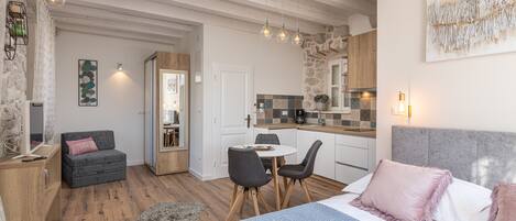 A modern, well-lit room with a bed, a dining table with chairs, a sofa, and a kitchen area.