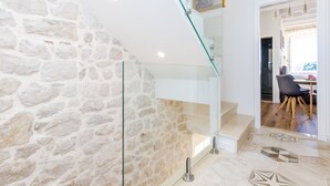 Un interior moderno con pared de piedra, una escalera de cristal y un comedor con mesa y sillas.