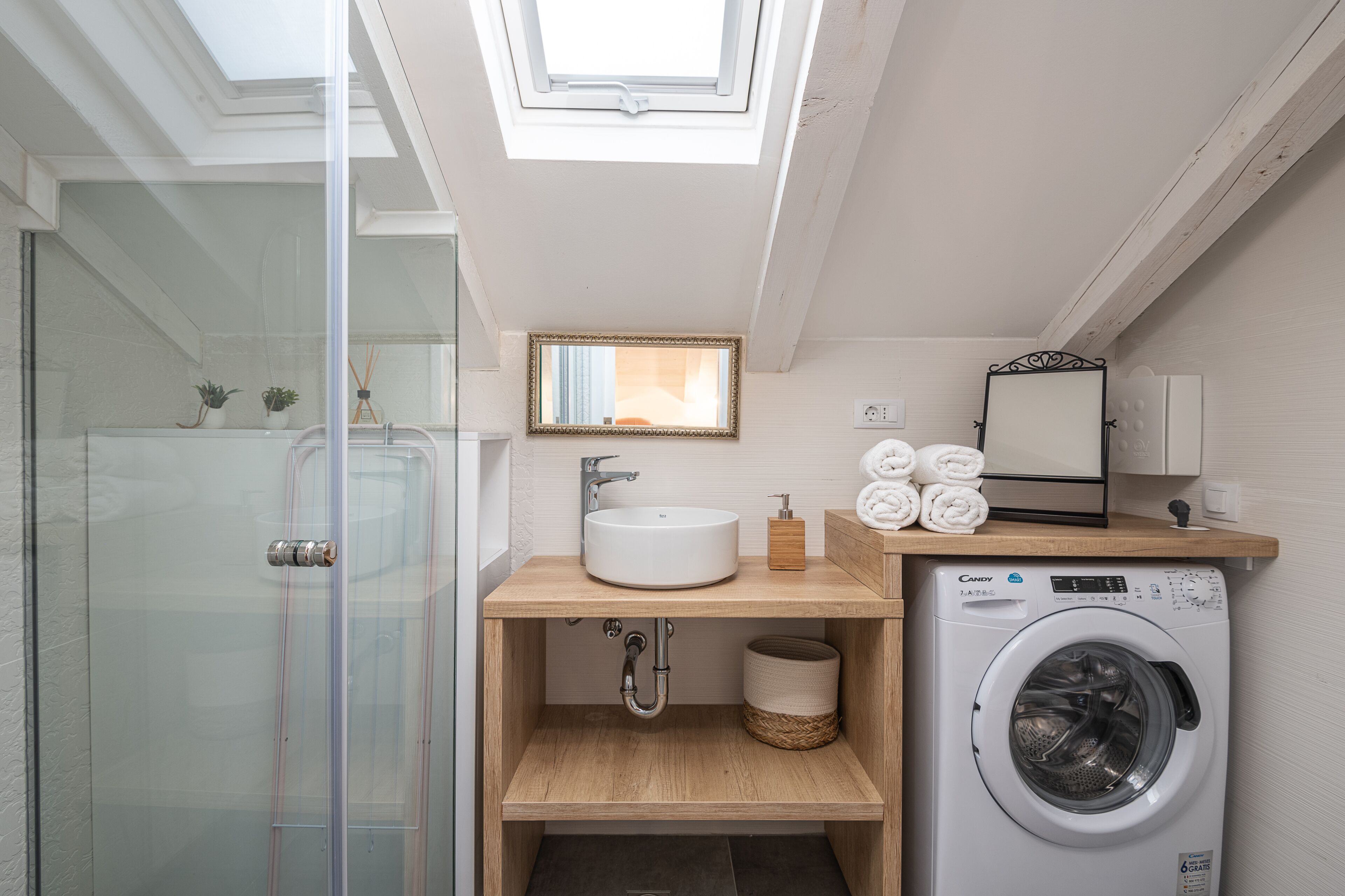 A modern bathroom with a skylight, a sink, a mirror, a towel rack, and a washing machine.