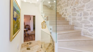 Una escalera con barandillas de vidrio que lleva a una habitación con pared de piedra y un cuadro en la pared.