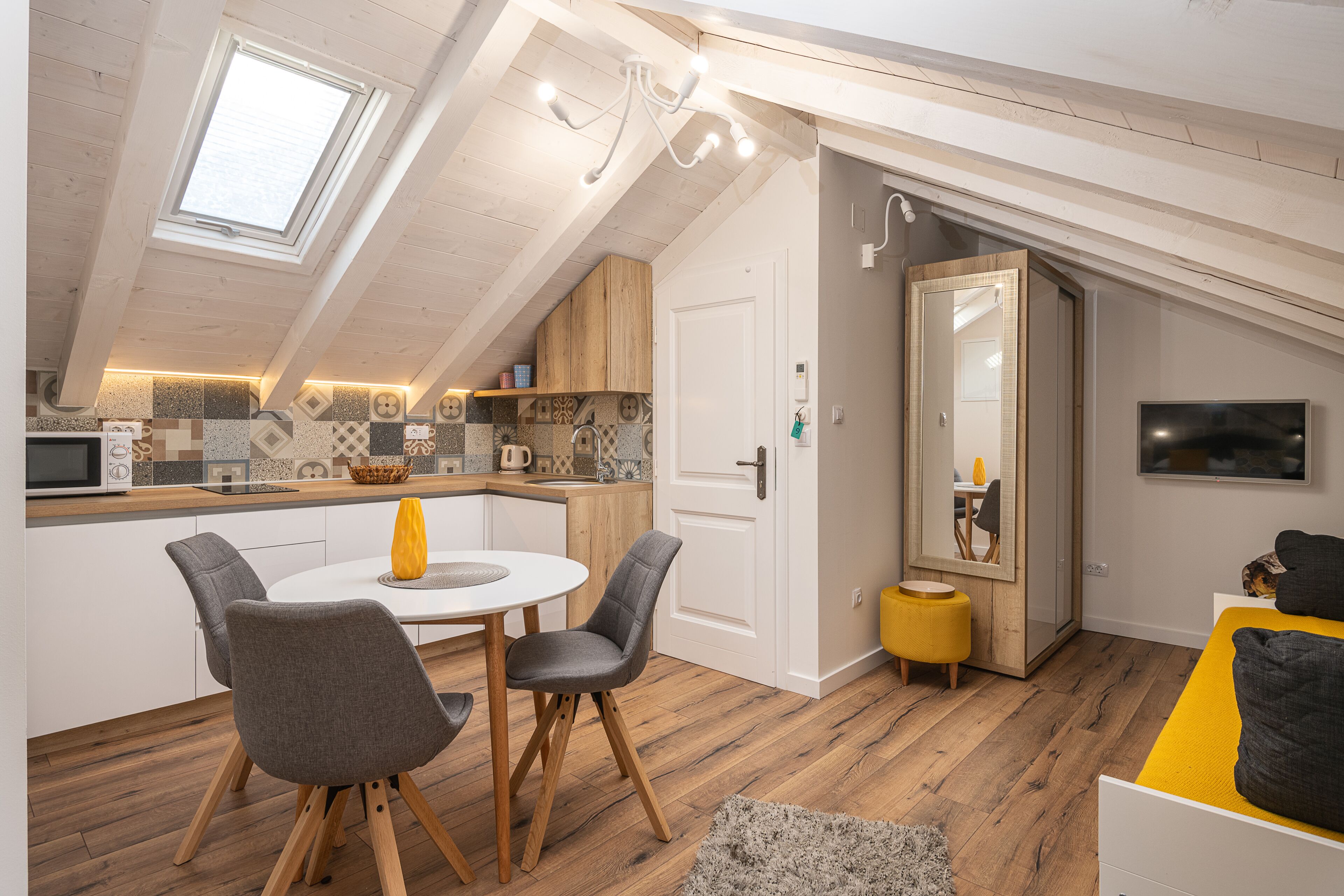 Un apartamento moderno y funcional con cocina, comedor y sala de estar. Cuenta con tragaluz, vigas de madera y televisor fijado a la pared.