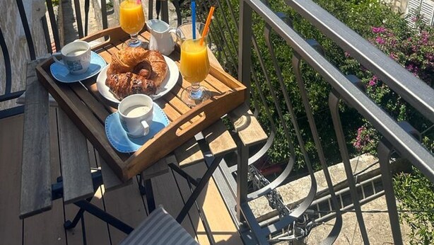 Un balcón con mesa dispuesta para el desayuno, con vistas a una zona costera con edificios y árboles.