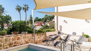 Zona junto a la piscina con sillones de descanso, una mesa y un muro de piedra.
