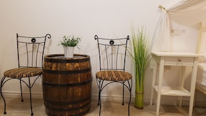 To metalstole med polstrede sæder, en træfad med en potteplante, og en høj grøn plante ved siden af et hvidt bord og en stol.