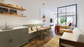 Eine moderne Küche mit Holzausstattung, ein Essbereich mit Holztisch und -stühlen, eine Sitzecke und ein großes Fenster mit Blick auf Grünflächen.