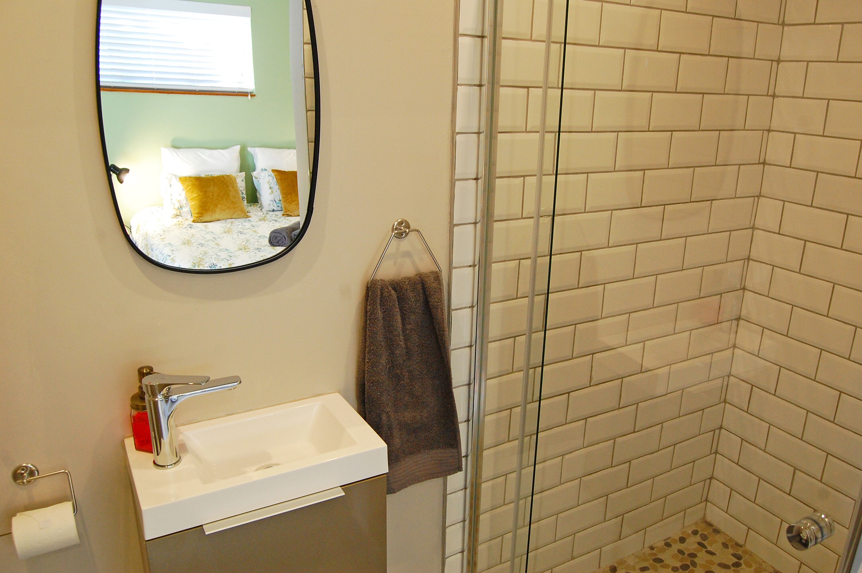 A bathroom with a sink, mirror, towel rack, and shower area.