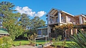 A two-story stone building with a balcony, surrounded by a well-maintained garden and trees. - Stonehaven Guest House (Clarens)