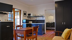 A compact kitchen with a dining area, featuring dark cabinetry, a microwave, and a small island. - Stonehaven Guest House (Clarens)