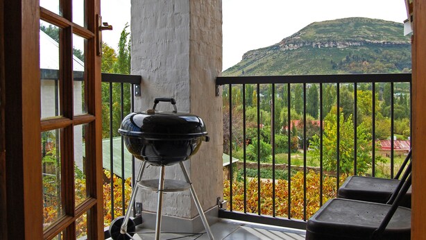 A balcony with a grill, a chair, and a view of a hill. - Stonehaven Guest House (Clarens)